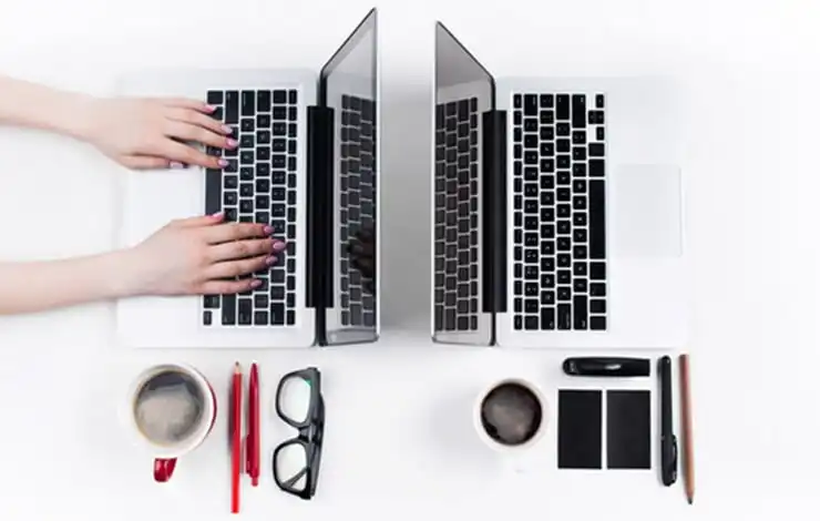 Two mirrored laptops with notebooks and coffee symbolizing a content hub strategy setup