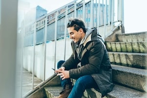 Man sitting on step using smartphone smiling