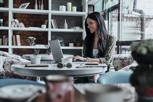 Putting fresh content into her blog. Attractive young smiling woman using laptop while sitting in restaurant