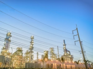 Brightly lit refinery with high-tension power lines at dusk