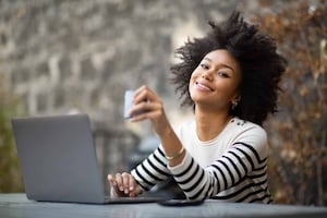 Happy young african woman sitting at cafe with laptop