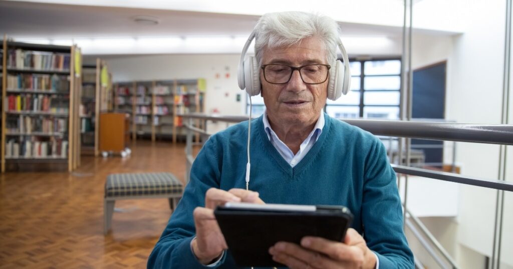 Older man using headphones to search website on tablet