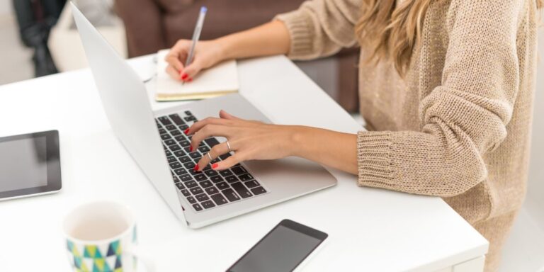 Woman working on laptop and taking notes at a white desk, symbolizing the process of refining and simplifying website content