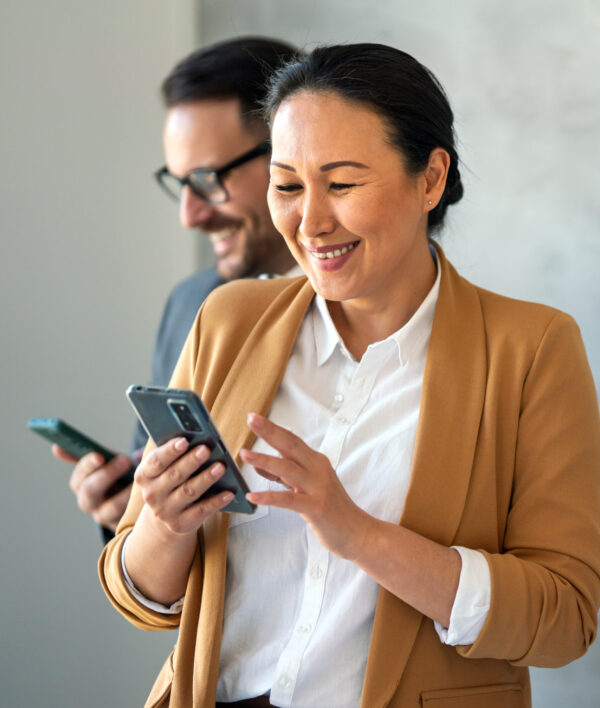 Smiling professionals engaged with their phones, demonstrating consistent online presence and digital engagement