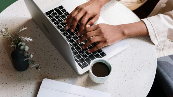 Close-up of hands typing on a laptop with a cup of coffee, symbolizing consistent online engagement and brand presence