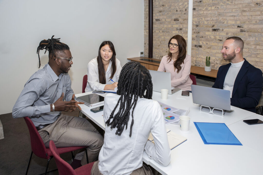 Multi-ethnic team of professionals engaged in a meeting, discussing online reputation management strategies, with laptops and documents on a conference table.