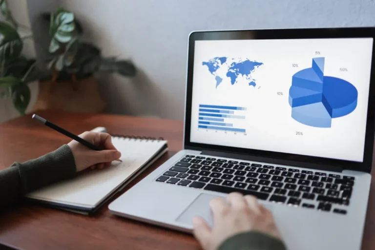 Person reviewing website analytics on a laptop screen showing bar and pie charts with global map data.