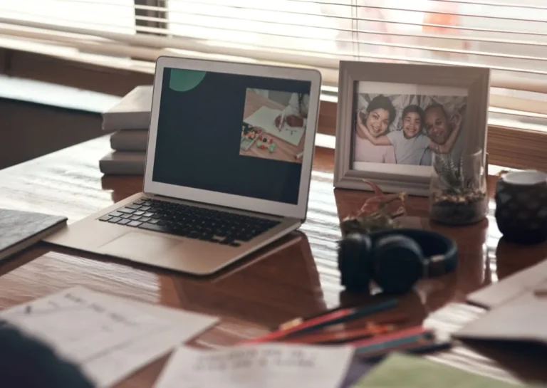 A cozy workspace showing a laptop, family photo, books, headphones, and notes—suggesting balance between work and personal life.