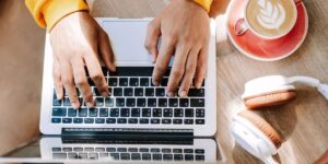 Person typing on a laptop with coffee and headphones on the desk, representing blogging and content creation.