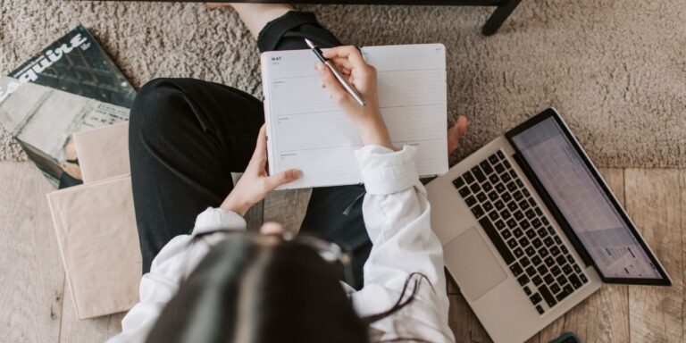 Person sitting on the floor with a laptop and open notebook, planning content and personal brand strategy to grow website traffic.