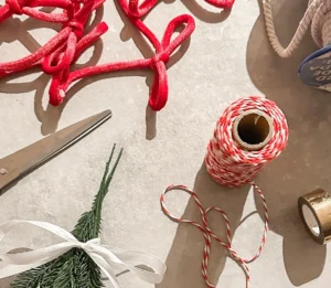 Flat lay of Christmas ribbon, twine, scissors, greenery, and festive wrapping supplies for holiday content creation.