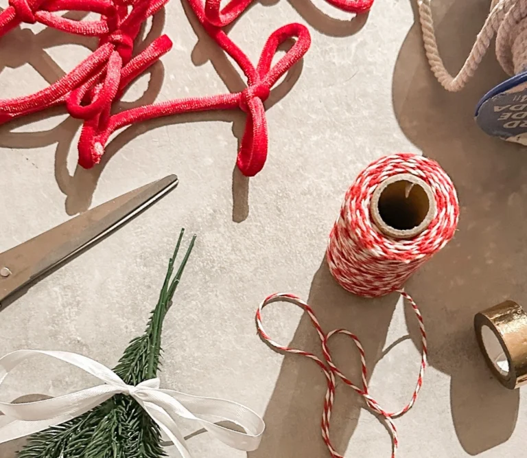 Flat lay of Christmas ribbon, twine, scissors, greenery, and festive wrapping supplies for holiday content creation.