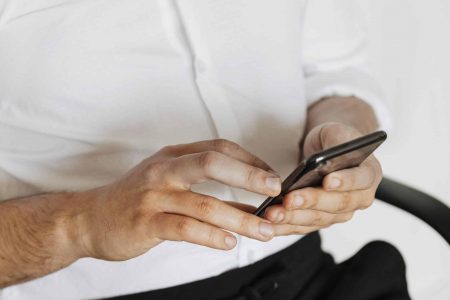 Close-up of man’s hands using Instagram on smartphone while seated in office chair