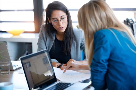 Two business women working together with laptop in the office. co-created content