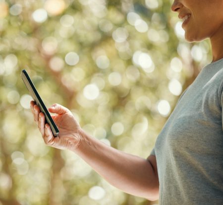 Person holding smartphone outdoors with blurred foliage in background