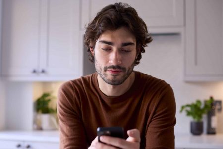 Young man analyzing Instagram metrics on his phone in a modern kitchen